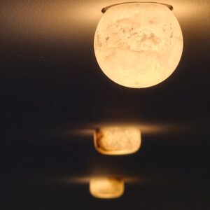 Frosted globe ceiling lamp emitting warm light against a dark background, with a row of blurred similar lamps below.