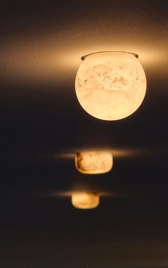 Frosted globe ceiling lamp emitting warm light against a dark background, with a row of blurred similar lamps below.