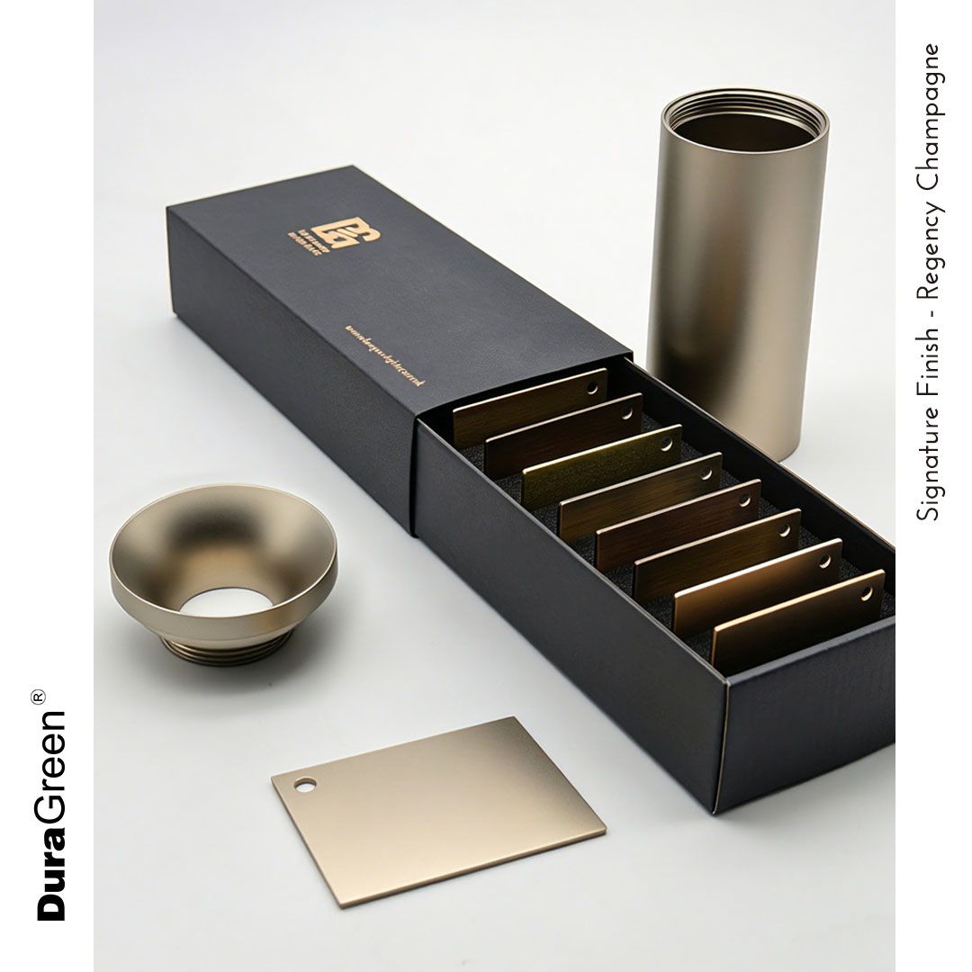 Kit of metal finish swatches in a black presentation box, displaying various bronze champagne tones (Regency Champagne); metal cup, cylindrical piece, and a small tag-like plate nearby.