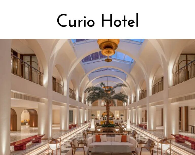 Interior of a luxury hotel lobby with tall arches, white columns, and a central palm tree