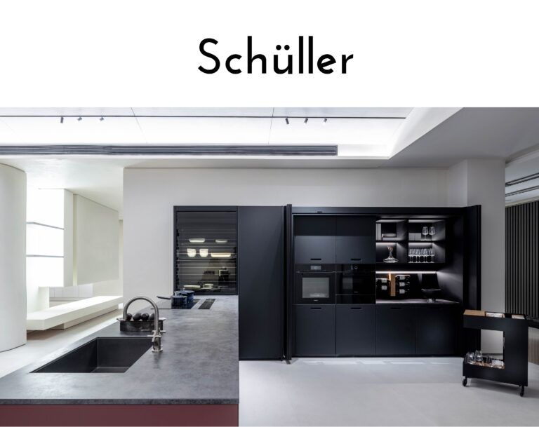 Brand showroom banner reading 'Schüller' above a modern black kitchen display with integrated ovens and glass-front cabinetry