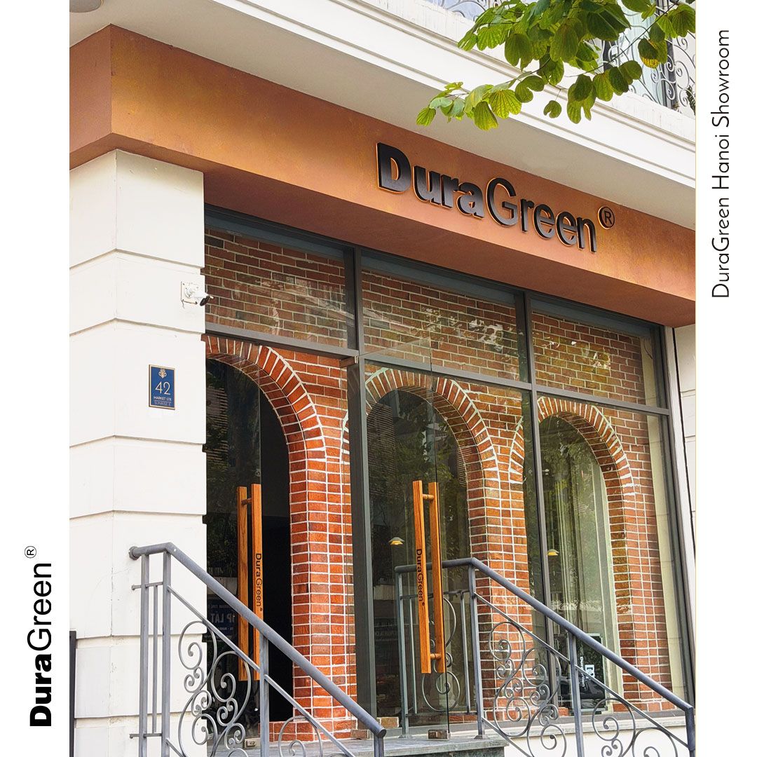 DuraGreen showroom storefront with brick arches, glass doors, wooden handles, and decorative metal railing on the stairs.