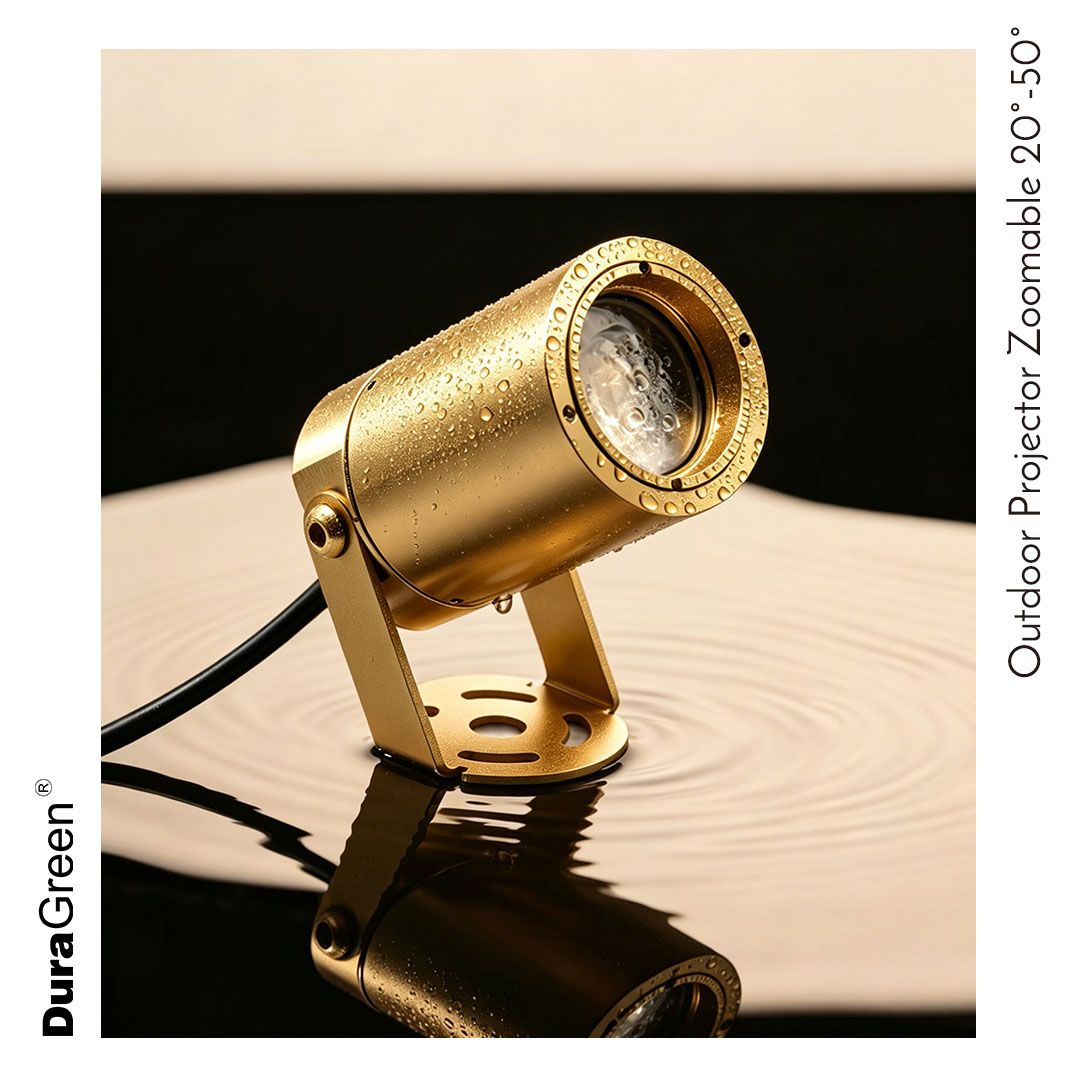 Gold outdoor projector/light on a hinged stand, water droplets on its body, resting on a reflective surface.