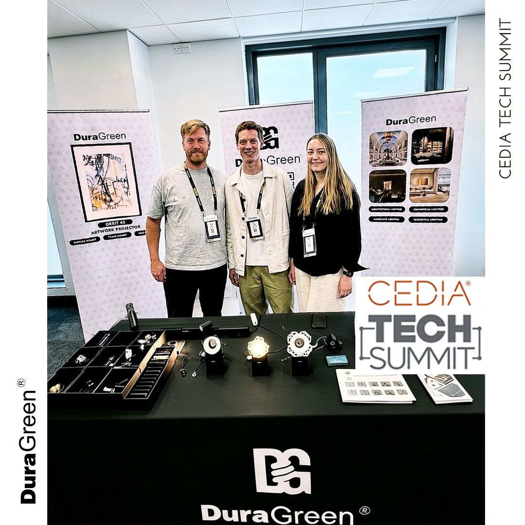 Three attendees stand behind a展示 booth with DuraGreen banners at a tech summit, products laid out on a table in front.